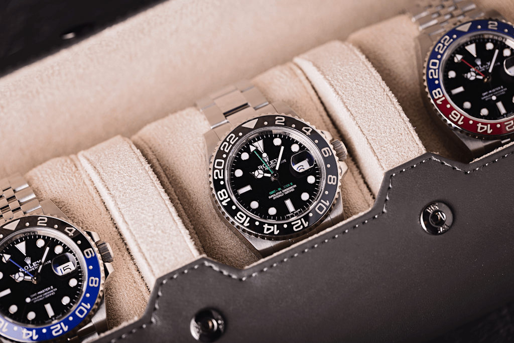 Three Rolex GMT-Master II watches with black dials and ceramic bezels displayed in a beige leather watch roll, featuring the black-and-blue &lsquo;Batman&rsquo; and black-and-red &lsquo;Pepsi&rsquo; bezel variants.