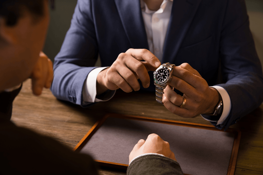 Luxury watch dealer showing a Rolex GMT-Master II stainless steel sports watch to a client during a consultation at Bob&rsquo;s Watches.
